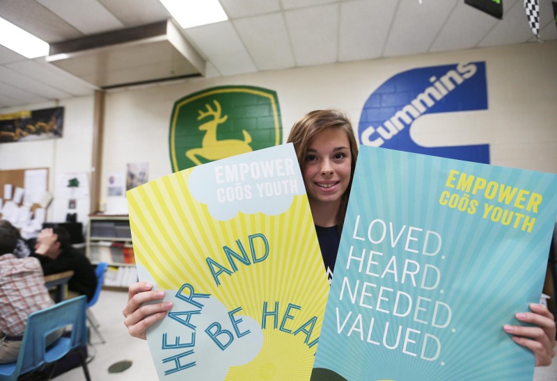 A teen poses with posters for Empower Coös Youth. Photo by Cheryl Senter.