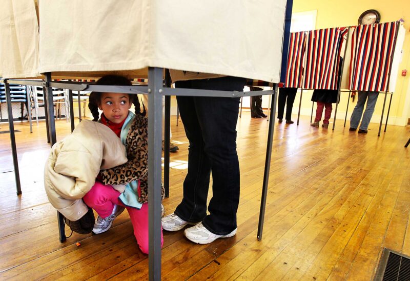 New Hampshire voter at the polls, with little girl waiting under the booth. (Photo by Cheryl Senter.)